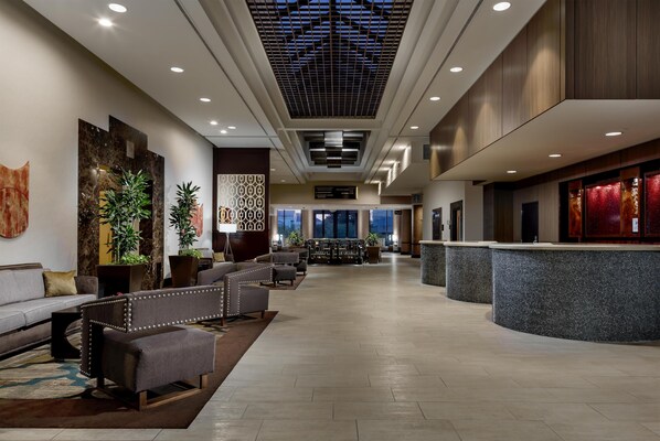 A hotel lobby with a reception desk, seating area, and large windows. - Hilton Charlotte University Place (Charlotte)