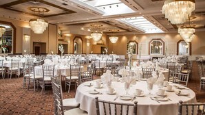 Un amplio salón de banquetes con mesas redondas dispuestas para comer, con candelabros y un techo alto con tragaluces.
