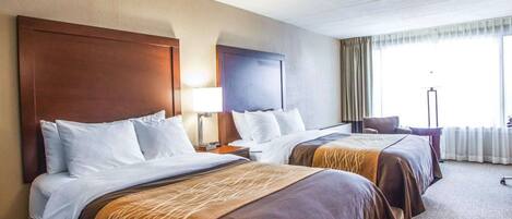 A hotel room with two beds, a nightstand with a lamp, a chair, and a large window with curtains.