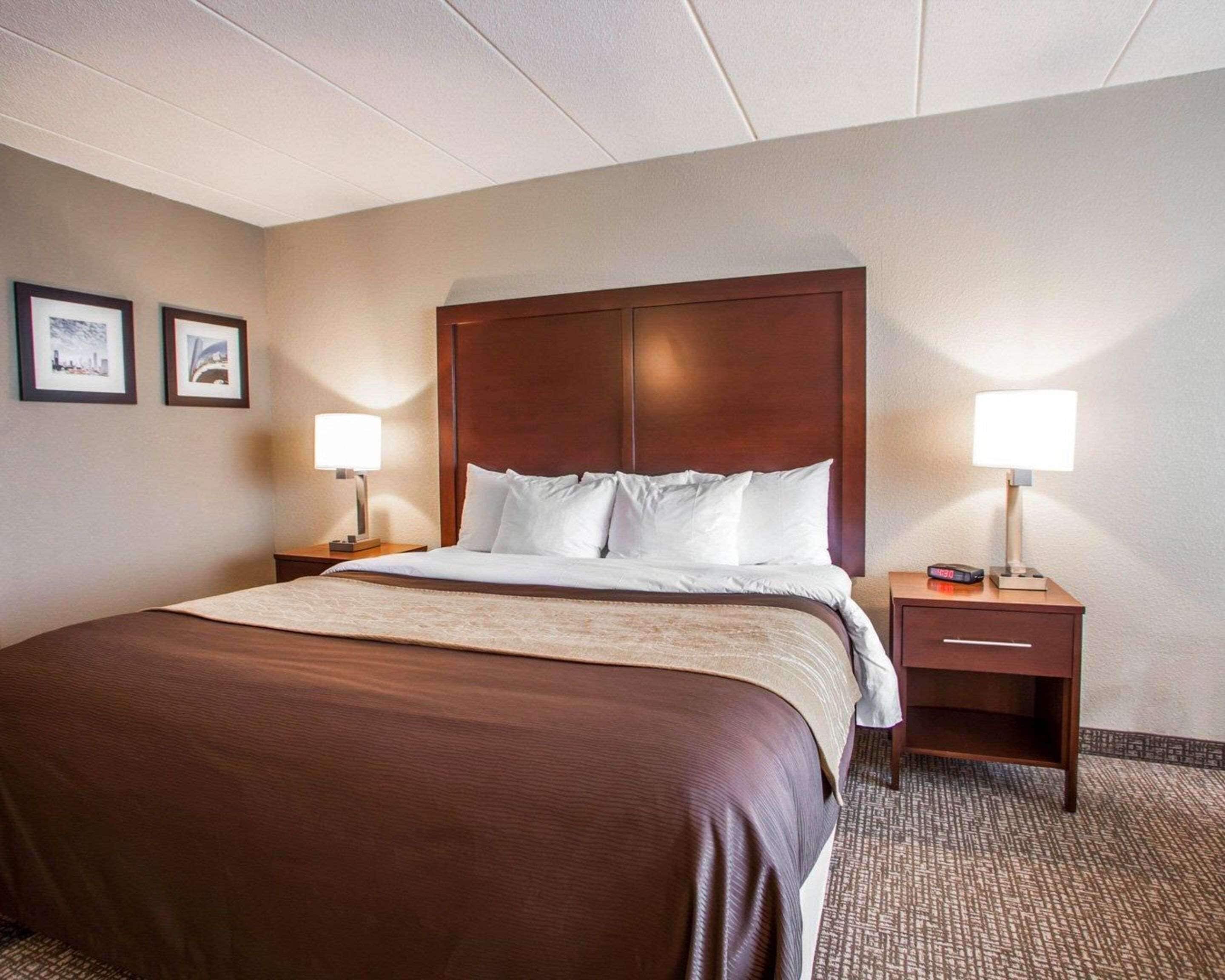 A hotel room with a large bed, two bedside tables, a nightstand, and a wall-mounted lamp.