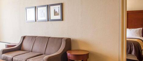 A hotel room with a brown sofa, a small round table, and a bed with a wooden headboard. There are three framed pictures on the wall.