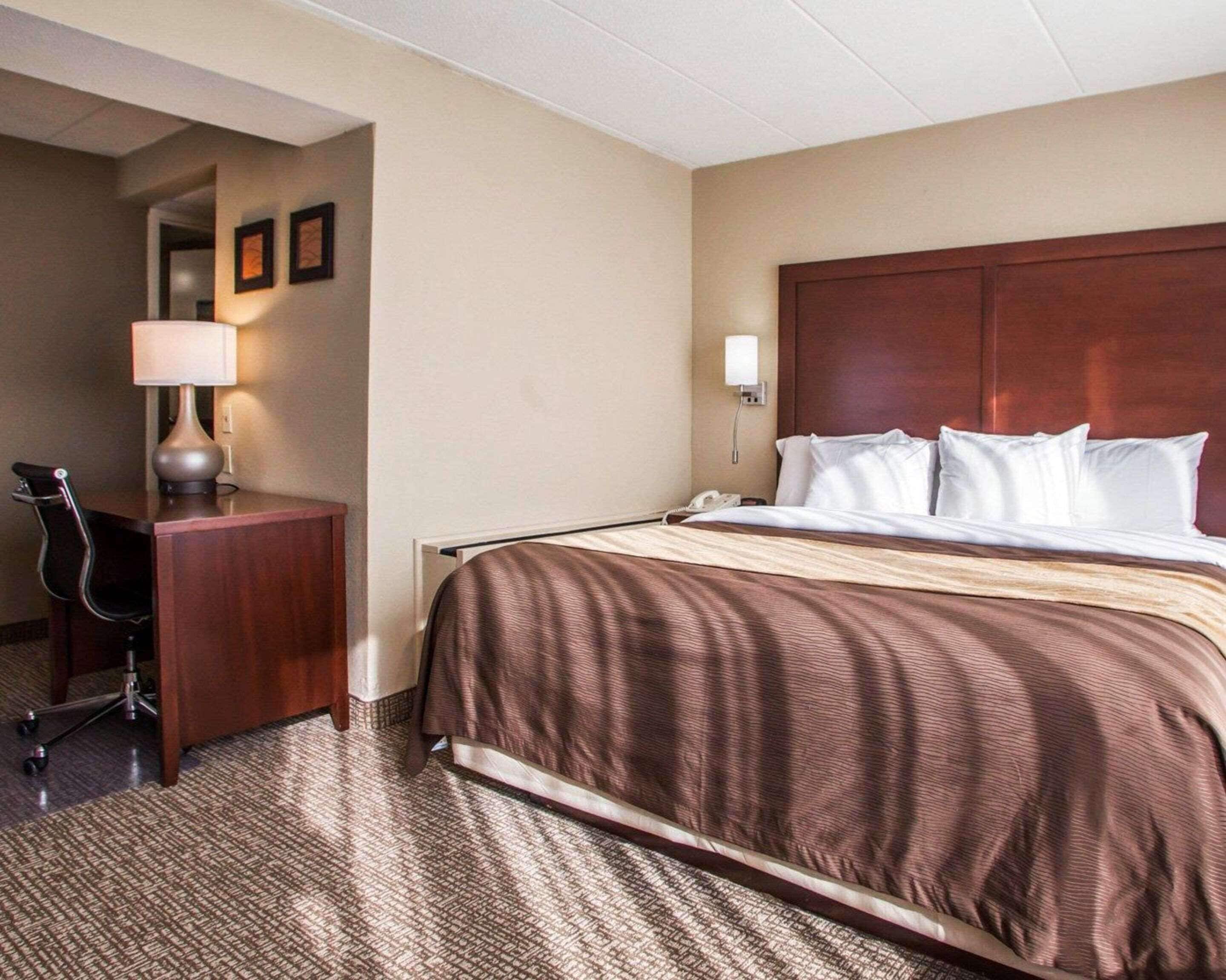 A hotel room with a large bed, a desk with a lamp, and a chair.