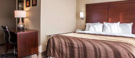 A hotel room with a large bed, a desk with a lamp, and a chair.