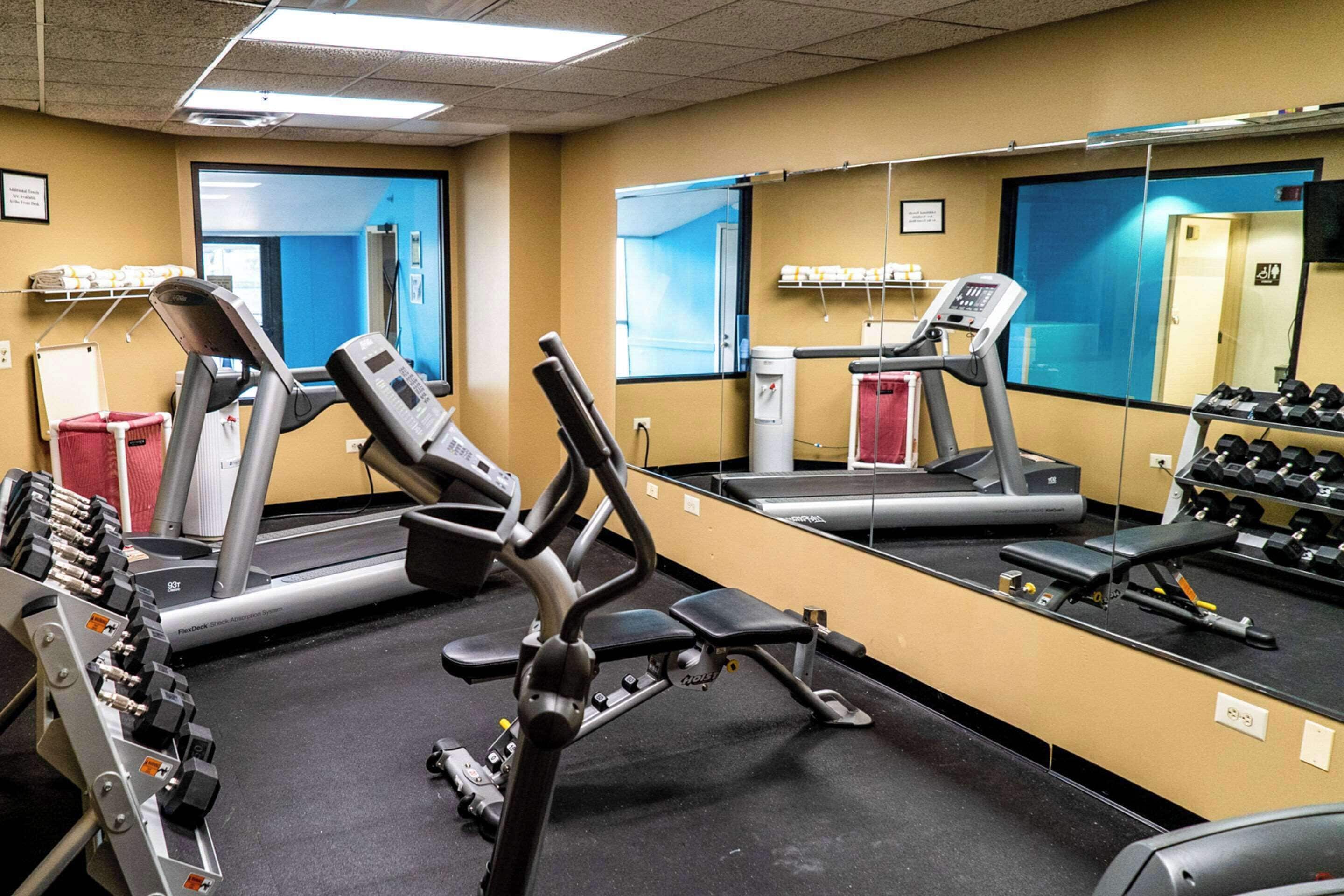 A gym with exercise equipment, a treadmill, and a mirror reflecting the space.