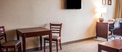 Una habitación de hotel con una mesa de madera, dos sillas, un televisor montado en la pared, un escritorio con una lámpara y una alfombra pequeña.
