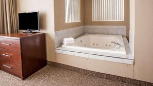 Un baño de hotel con una bañera grande, un aparador de madera con cajones y un televisor de pantalla plana encima.