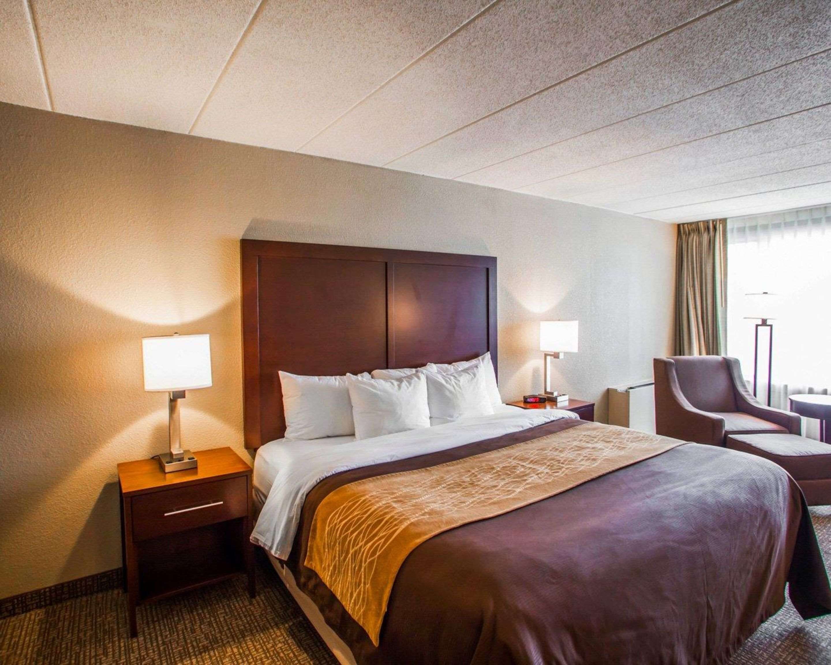 A hotel room with a large bed, two bedside tables with lamps, a chair, and a window with curtains.
