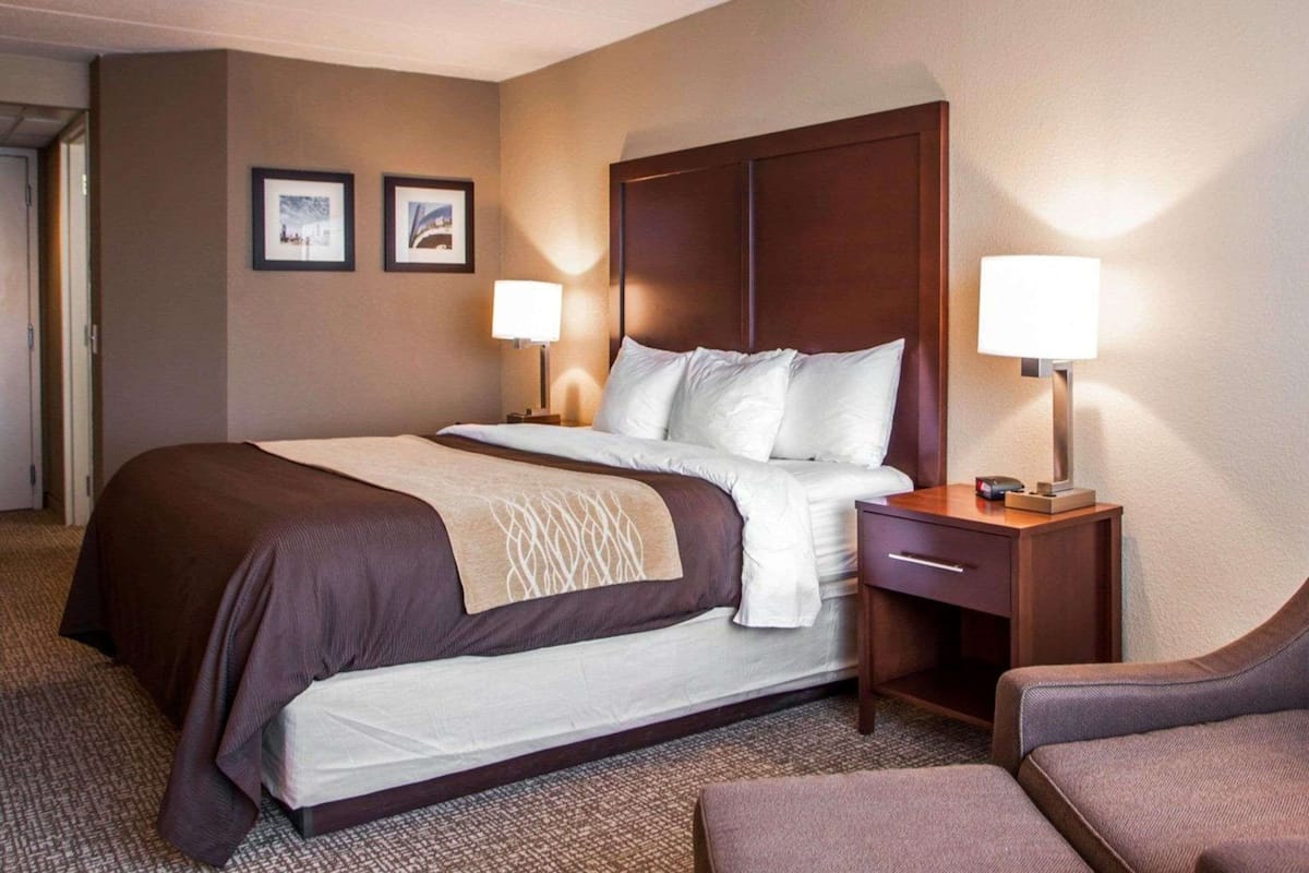A hotel room with a large bed, two bedside tables with lamps, a chair, and two framed pictures on the wall.