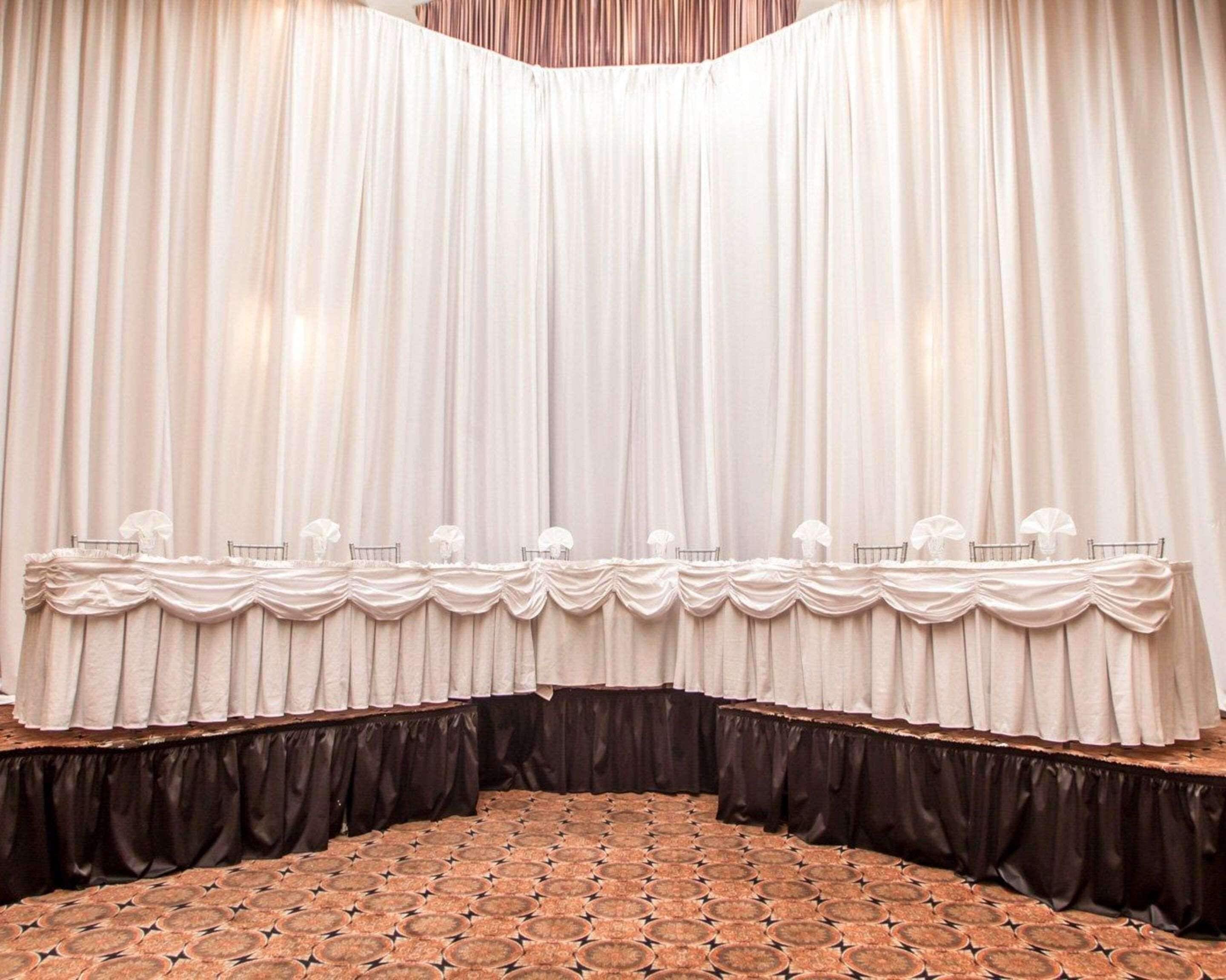 Une scène avec un décor constitué d’un rideau, une table entourée de chaises et un tapis à motifs.