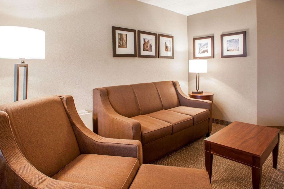 A hotel room with a brown leather sofa, a wooden coffee table, and a lamp on a side table. There are framed pictures on the wall.