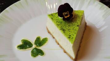 Ein Stück Käsekuchen auf einem weißen Teller, mit einer Zierblume darauf.