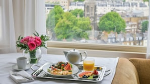 A breakfast tray with a plate of food, a glass of orange juice, a teapot, and a vase of pink flowers on a table by a window with a city view. - The Park Tower Knightsbridge, A Luxury Collection Hotel (London)