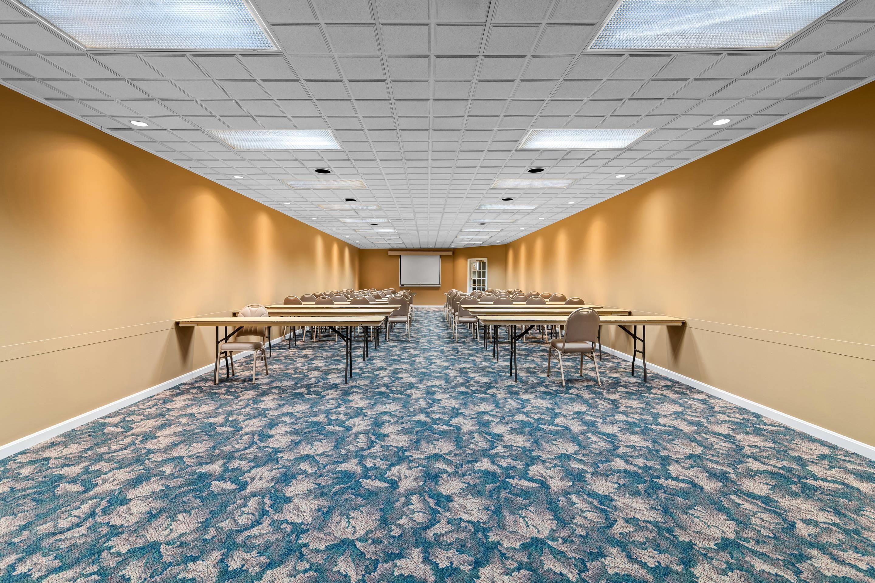 Un salón de conferencias con alfombra de diseño azul, paredes color beige y techo blanco con iluminación empotrada.