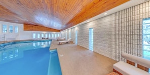 A swimming pool with lounge chairs, wooden ceiling, and tiled walls.