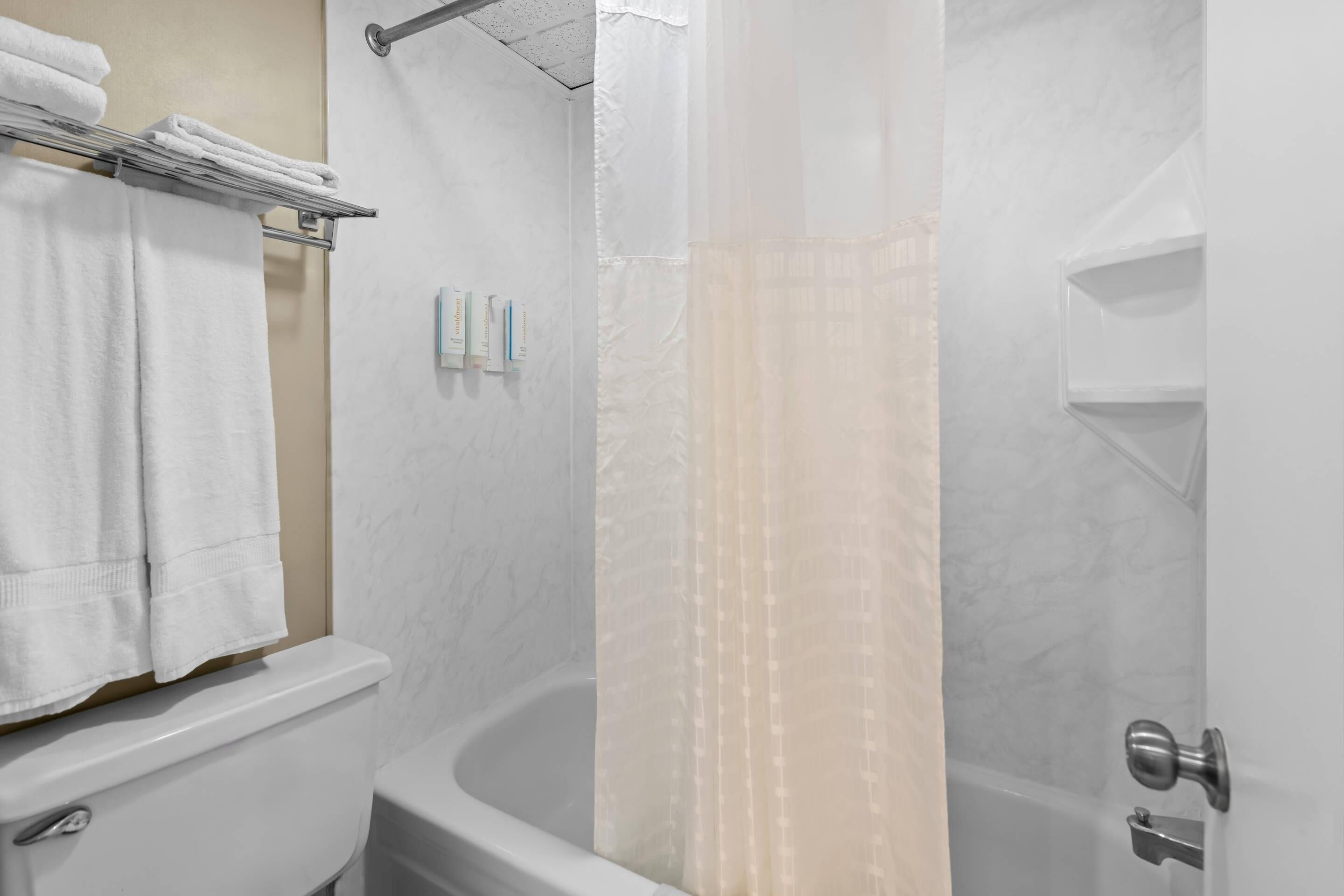 A bathroom with a toilet, a towel rack with folded towels, a shower curtain, and a shower area.