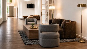 A modern living room with a sofa, armchair, and coffee table, a chandelier, and a television on the wall. - Clarion Hotel & Conference Center Lewiston (Lewiston)