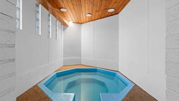 A corner room with a hexagonal pool, wooden ceiling, and white walls.