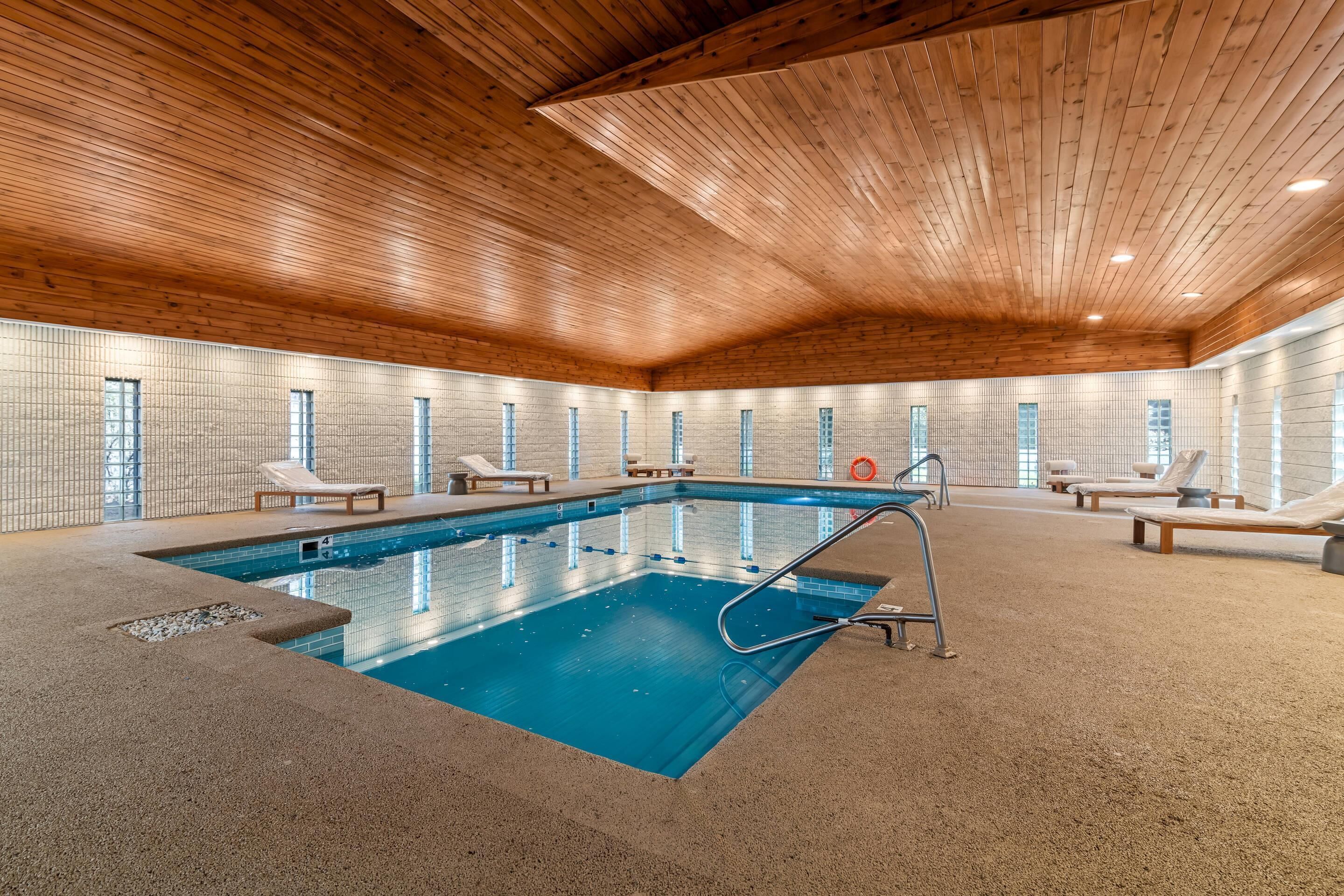 An indoor swimming pool with lounge chairs and a wooden ceiling.