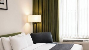 A hotel room with a bed, a chair, a lamp, a window with curtains, and an air conditioning unit. - Clarion Hotel & Conference Center Lewiston (Lewiston)