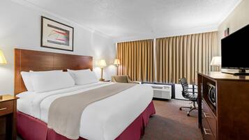 Een hotelkamer met een bed, bureau, stoel, televisie en airconditioning.