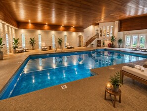 An indoor swimming pool with a wooden ceiling, lounge chairs, and potted plants.