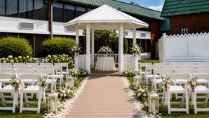 A gazebo with white chairs and tables arranged in a semi-circle, a wooden pathway with white flower petals, and a building with a green roof in the background. - Clarion Hotel & Conference Center Lewiston (Lewiston)