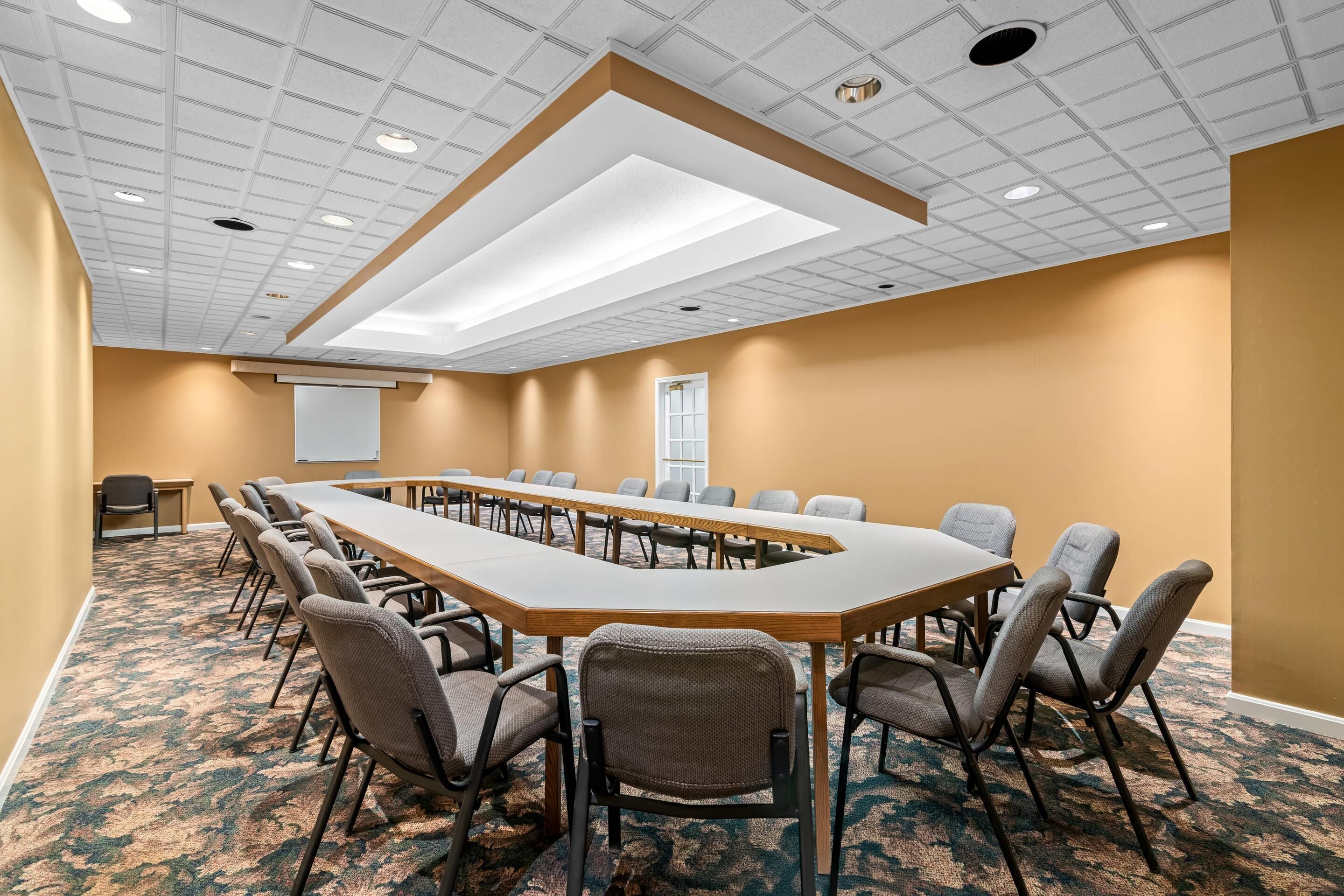 A conference room with a long table, chairs, carpeted floor, and a whiteboard.