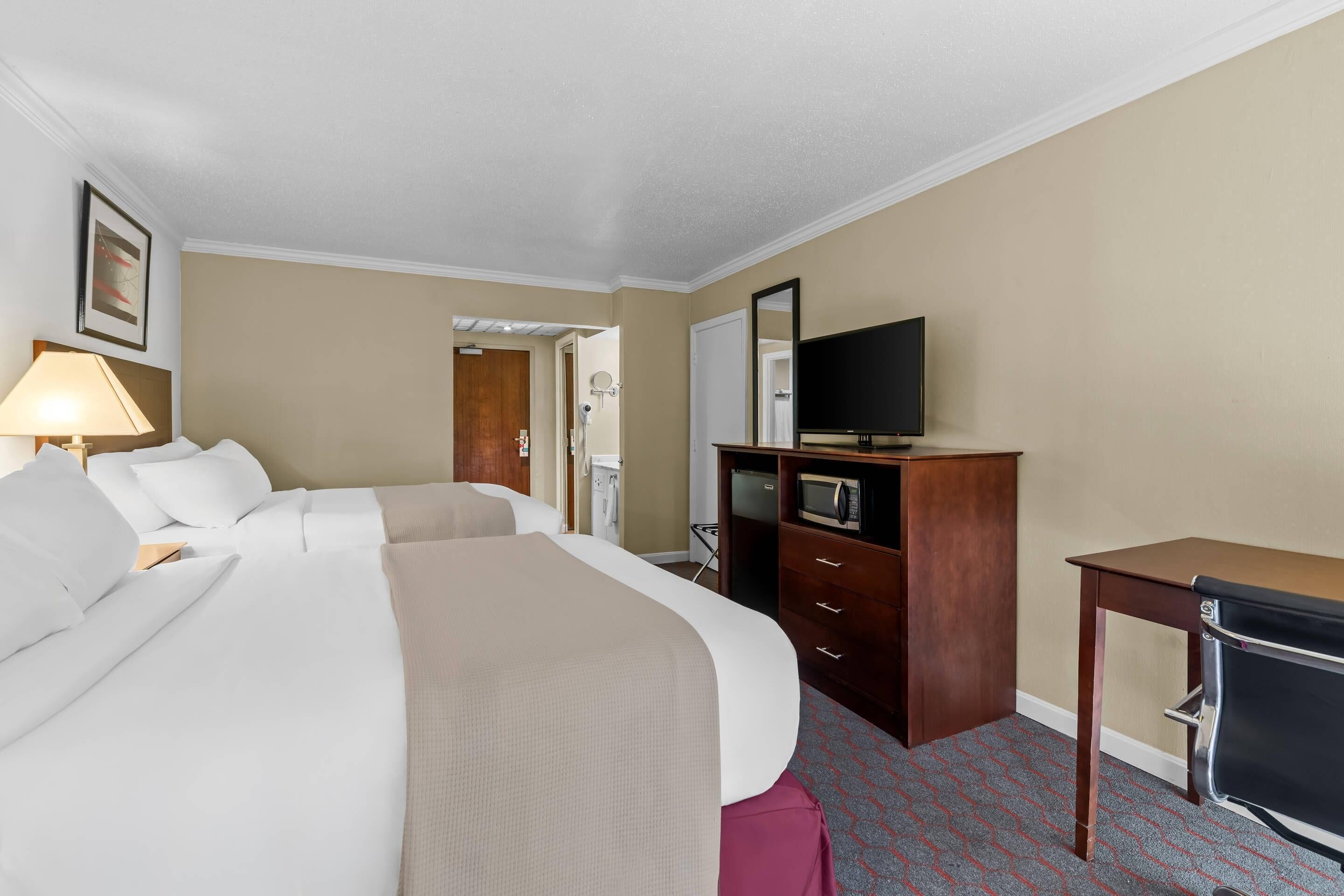 Une chambre d’hôtel équipée d’un lit, d’un bureau, d’une télévision, d’un miroir et d’un four à micro-ondes.