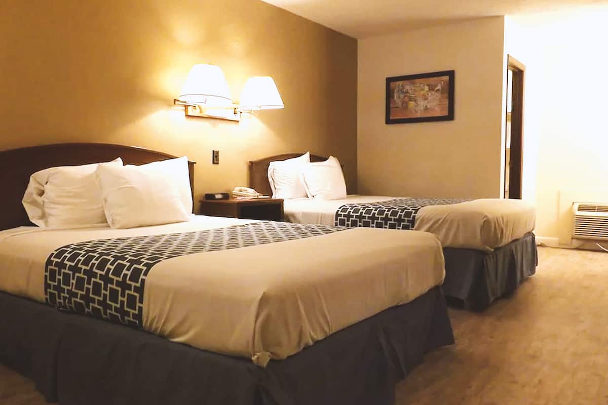 A hotel room with two beds, each with a patterned bedspread and pillows. There are wall-mounted lamps above the beds and a framed picture on the wall.