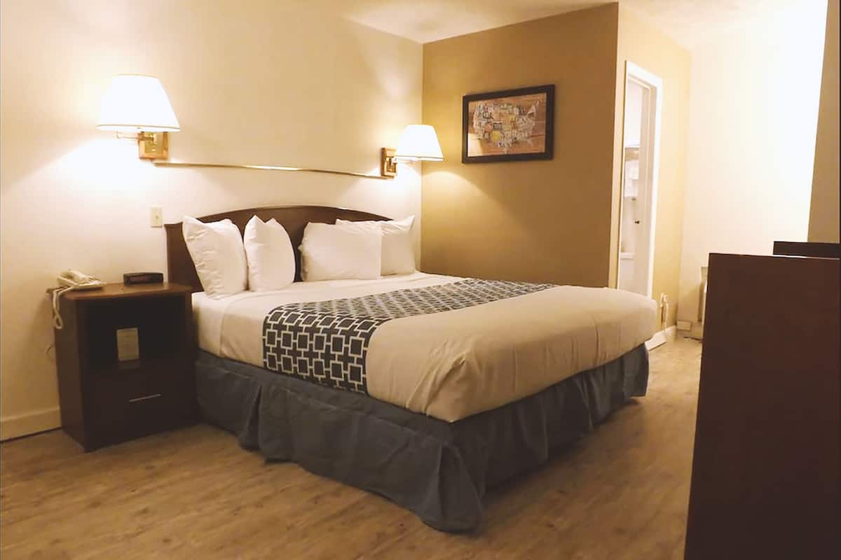 A neatly made bed with a patterned bedspread, two bedside lamps, a nightstand with a phone, and a framed picture on the wall.