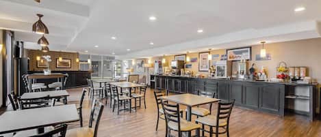 A spacious dining area with wooden tables and chairs, a kitchen counter with various appliances, and pendant lighting.