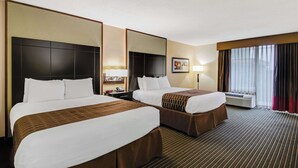 A hotel room with two beds, a large mirror, a nightstand, a lamp, and a window with curtains. - Best Western Inn of Del Rio (Del Rio)
