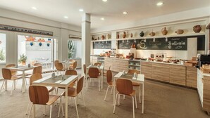 Un interior de restaurante con mesas y sillas de madera, un menú en una pizarra y una variedad de cerámica exhibida en estanterías.