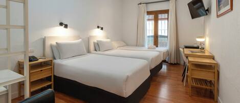 Una habitación de hotel con dos camas, un escritorio, una silla, un televisor y una ventana con cortinas.