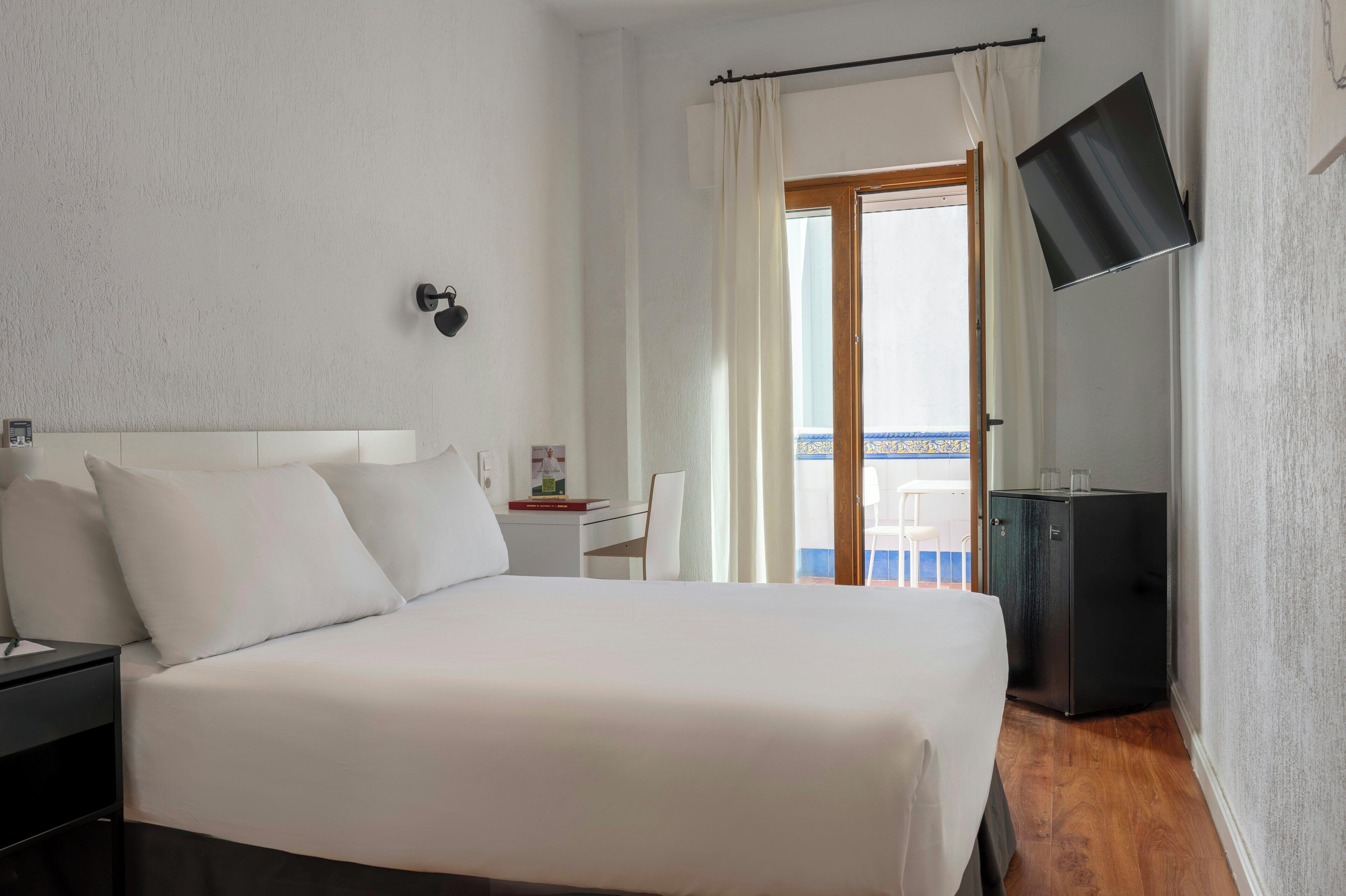 A hotel room with a bed, a desk, a chair, a TV, and a balcony view.