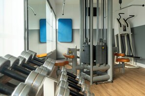 Un gimnasio con equipo de levantamiento de pesas, máquinas de ejercicio y un espejo.