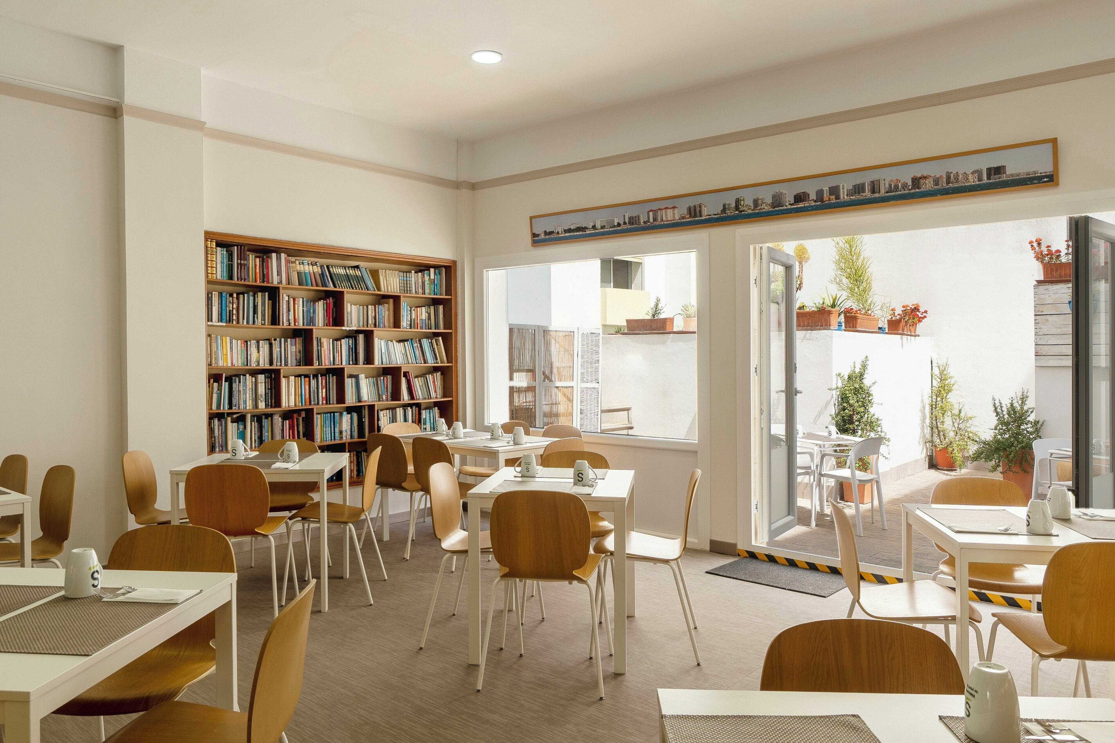 Une bibliothèque avec des étagères, des tables, des chaises et une vue sur l’extérieur.