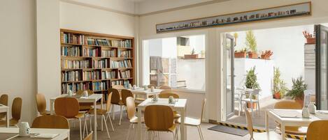 A library with bookshelves, tables, chairs, and a view of the outside.