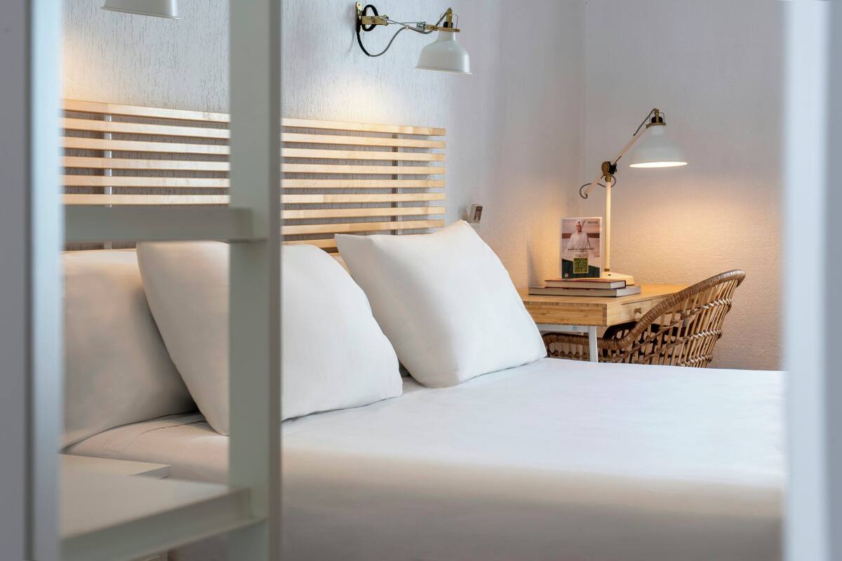 Una cama bien hecha con sábanas blancas, un cabecero de madera y dos lámparas de noche.