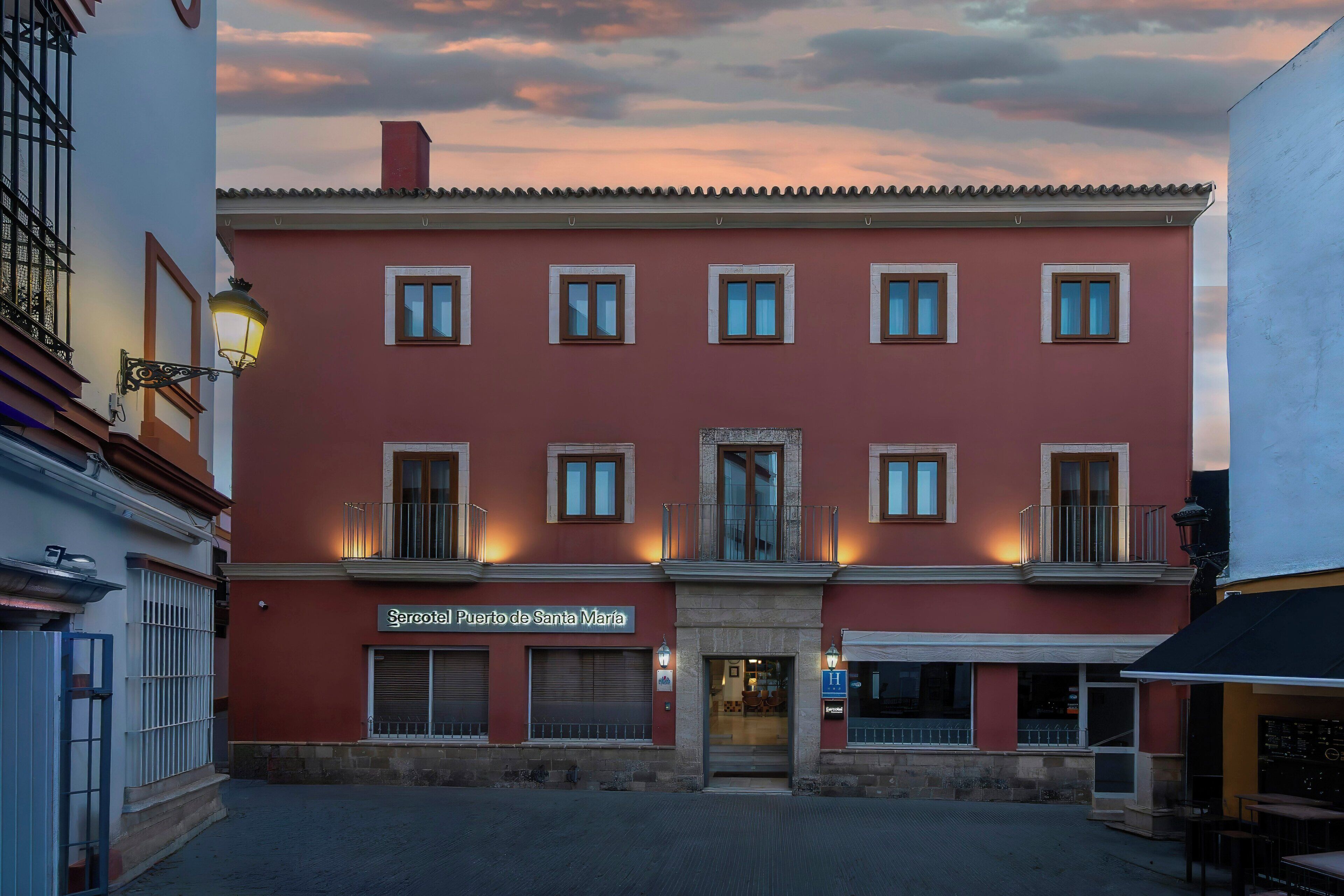 A red building with multiple windows, a sign reading 'Mercado de Santa Maria,' and a door with a sign above it.