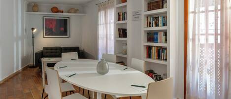 A dining area with a white table, chairs, a vase, and a bookshelf with books and decorative items.