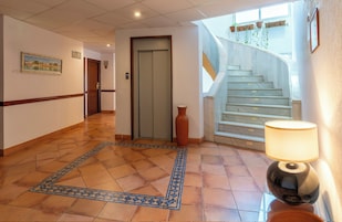 A hotel lobby with a tiled floor, a door, a staircase, and a wall-mounted lamp.