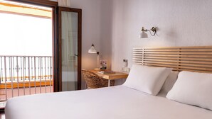Hotellihuone, jossa on sänky, työpöytä lampun kanssa, tuoli ja näkymä ulkoiselle parvekkeelle.
