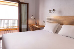 A hotel room with a bed, a desk with a lamp, a chair, and a view of the outside balcony.