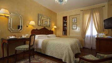 Quarto de hotel com cama, escrivaninha, cadeira, televisão e estante.