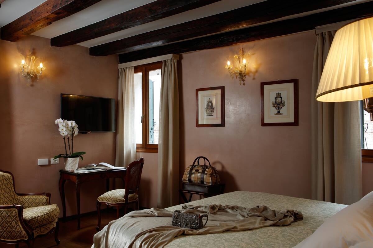 A hotel room with a bed, a desk with a chair, a television, and two wall sconces.