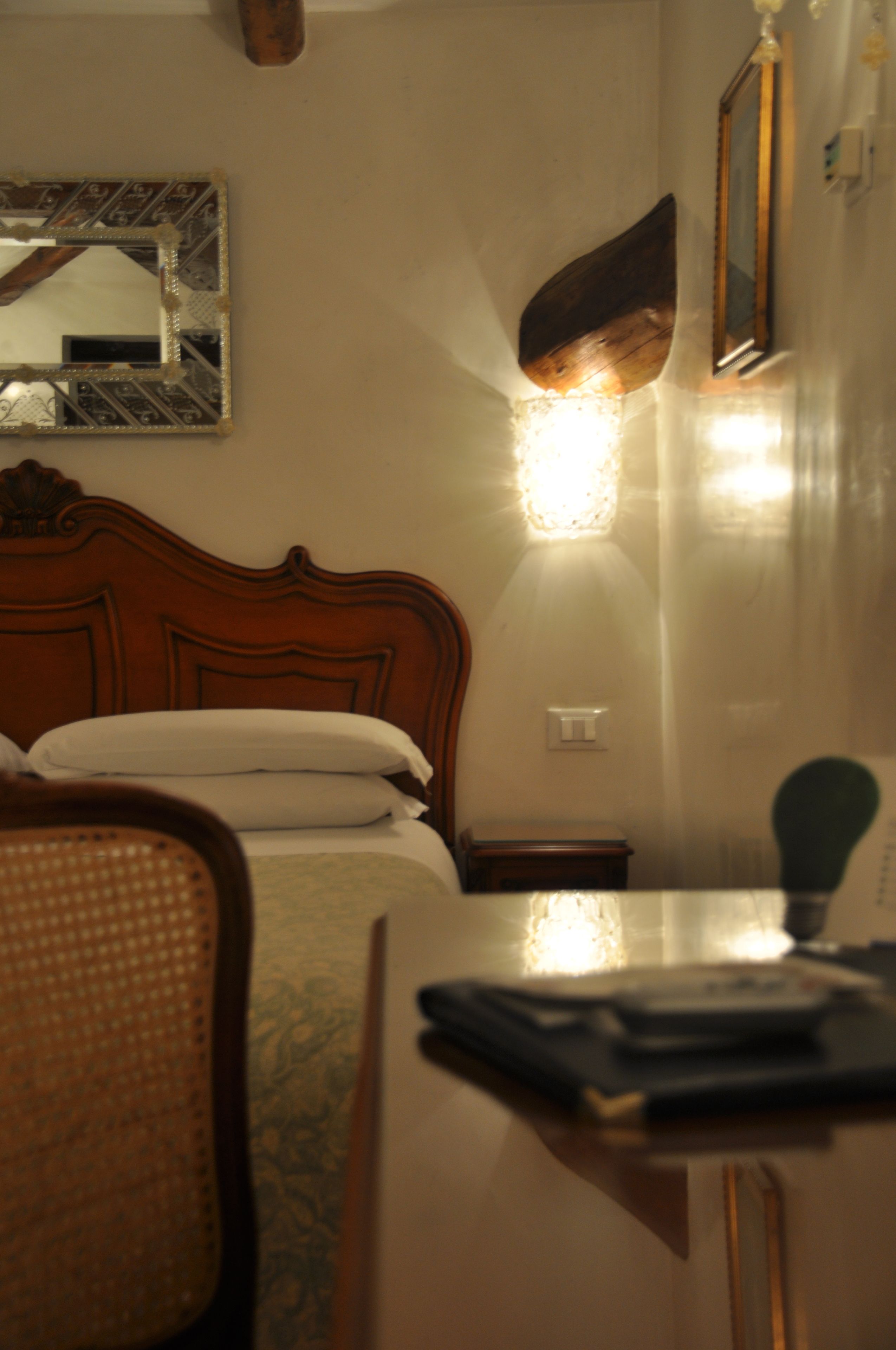 Une chambre d’hôtel avec un lit en bois, un miroir, une table de chevet et une chaise.