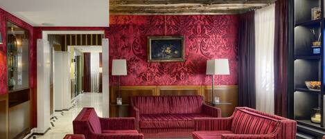 Un vestíbulo con papel tapiz rojo estampado, techo de madera y asientos tapizados en rojo.