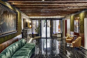 Un vestíbulo con un sofá de terciopelo verde, piso de mármol y techo de madera.