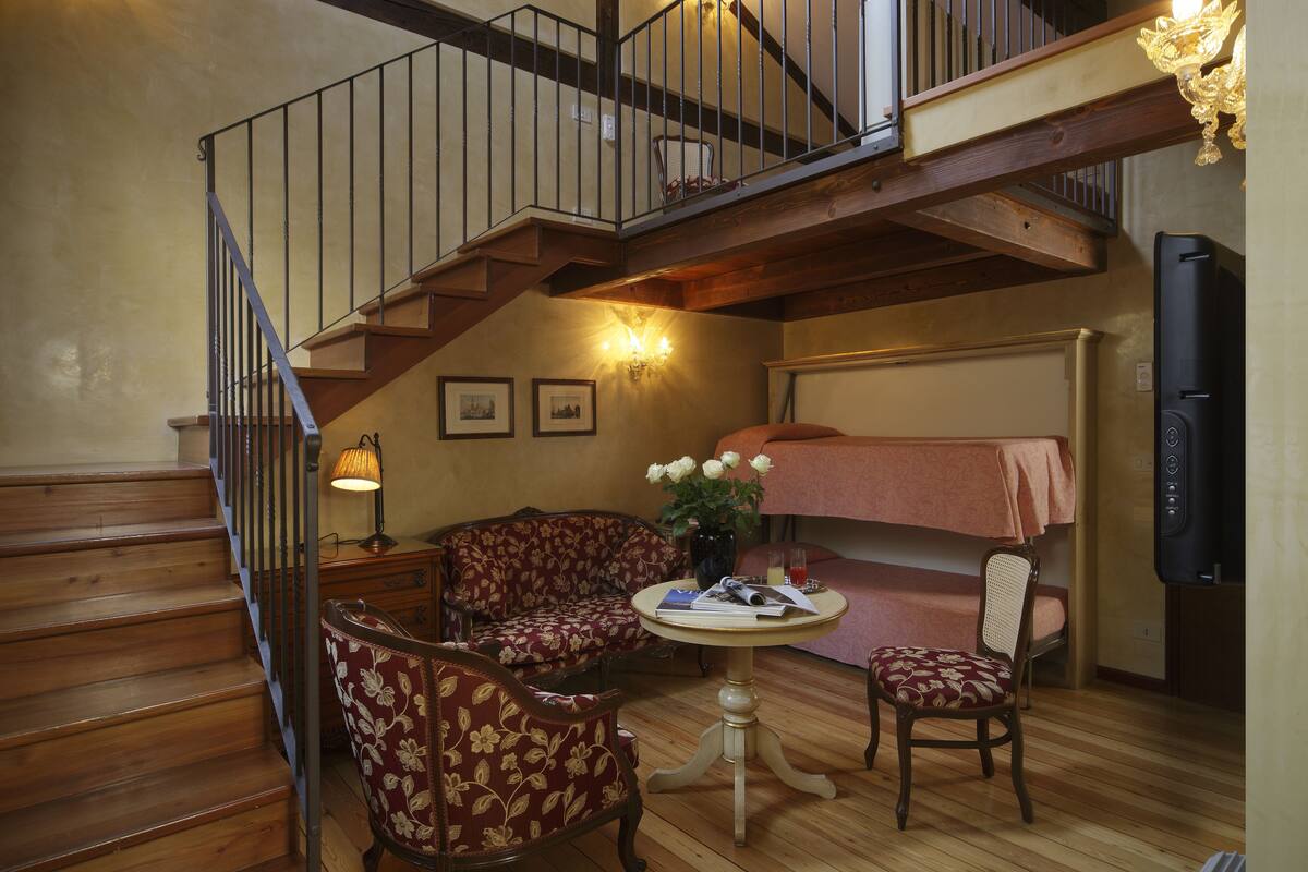 A cozy room with a wooden staircase, a sofa, a small table, and a bunk bed.